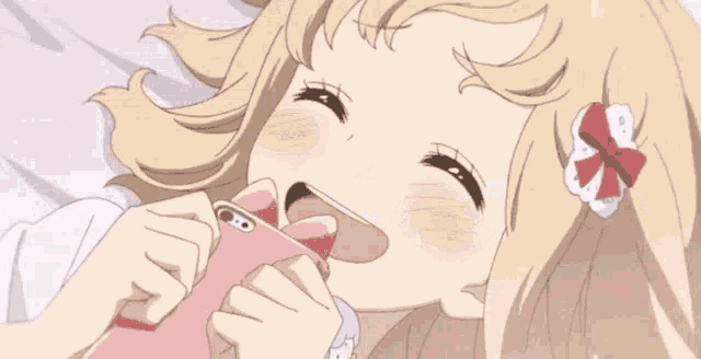 a blonde anime girl is laying on a bed holding a pink cell phone in her mouth .