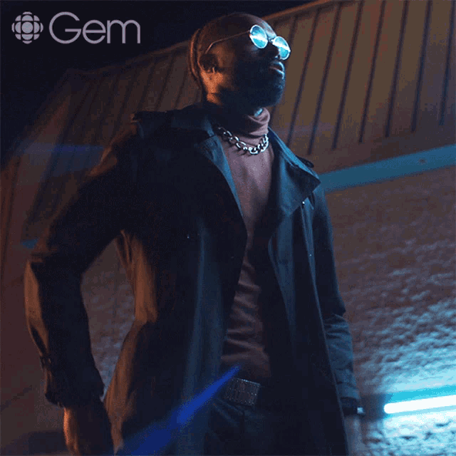 a man wearing sunglasses and a trench coat is standing in front of a gem logo