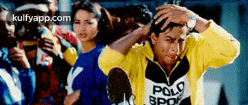 a man in a yellow polo shirt is holding his head while standing in front of a crowd of people .