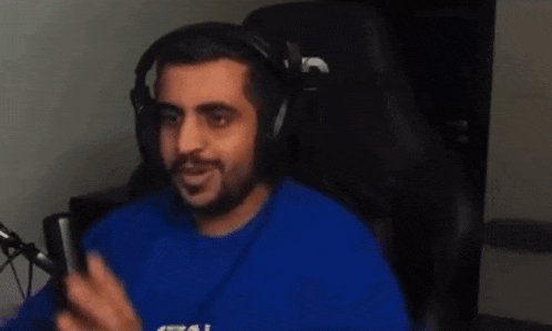 a man wearing headphones and a blue shirt is sitting in a gaming chair .
