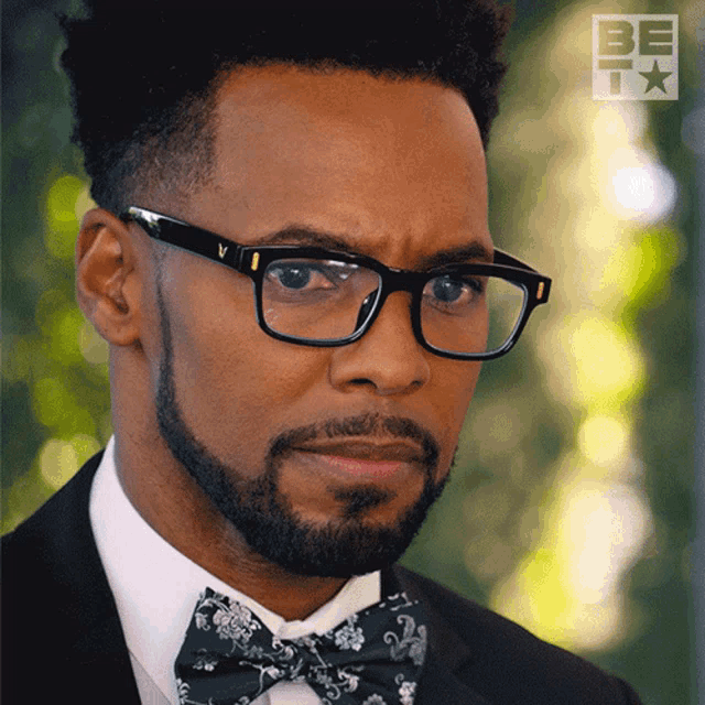 a man wearing glasses and a bow tie has the word be on the bottom right