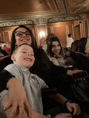 a woman with glasses sits next to a boy and a girl in a theater
