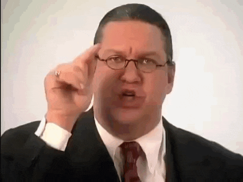 a man in a suit and tie is pointing his finger at his head .