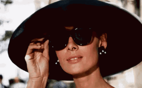 a woman wearing a hat and sunglasses adjusts her glasses