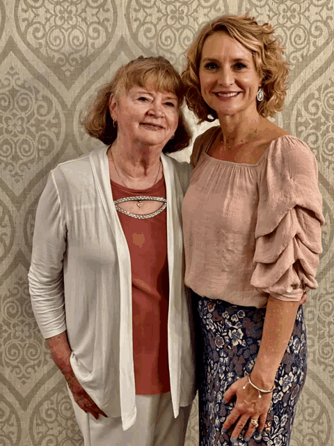 two women are posing for a picture in front of a wall