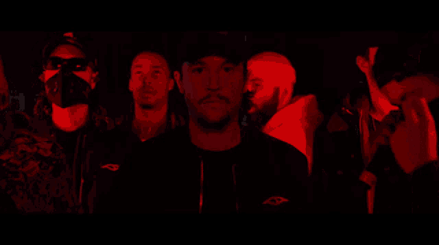 a group of men are standing in a dark room with red lights