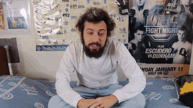a man is sitting on a bed in front of a poster for ufc fight night