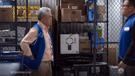 two men are standing next to each other in a store . one of the men is wearing a superstore vest .