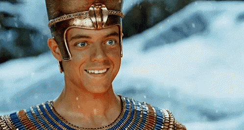 a man is wearing a helmet and smiling in front of a snowy mountain .