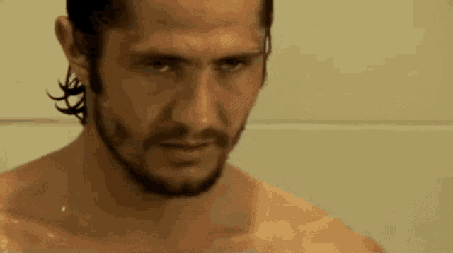 a shirtless man with a beard is taking a bath in a shower .