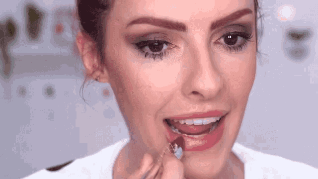 a woman is applying lipstick to her lips and smiling .