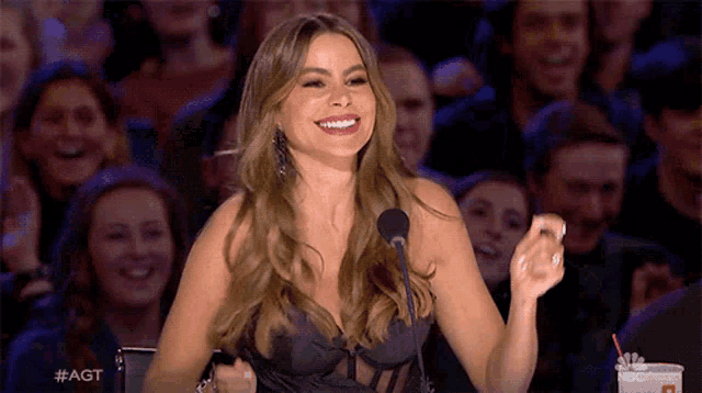 a woman in a black dress is speaking into a microphone and smiling .