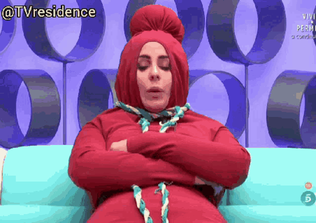 a woman in a red costume is sitting on a blue couch with her arms crossed and the words @tvresidence below her