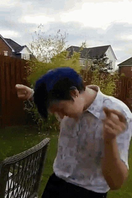 a man with blue hair is dancing in a yard