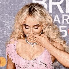 a woman in a pink dress is covering her mouth with her hands .