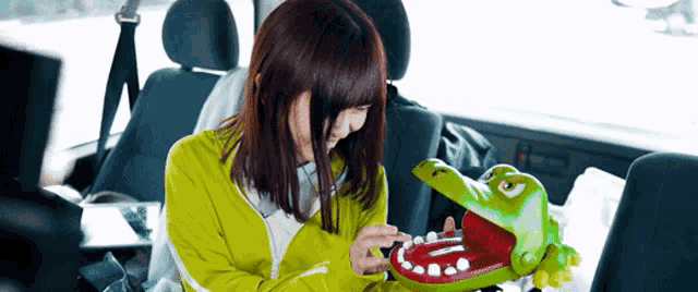 a woman in a green jacket is holding a toy crocodile with its mouth open