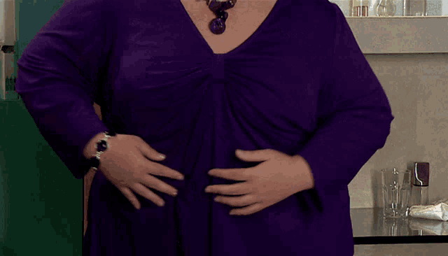 a woman in a purple top is holding her belly and wearing a watch