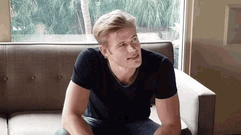 a man is sitting on a couch in front of a window looking at something .