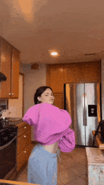 a woman is standing in a kitchen wearing a pink sweater and blue shorts .