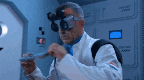 a man in a lab coat and goggles holds a small object in his hand