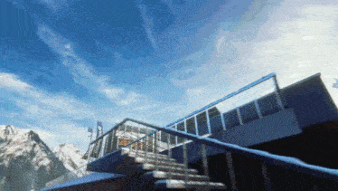 a building with stairs leading up to a balcony with mountains in the background and a blue sky