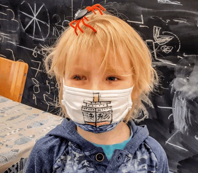 a young boy wearing a face mask has a spider in his hair