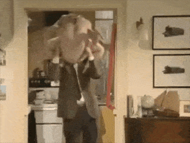 a man in a suit is holding a turkey over his head in a kitchen .