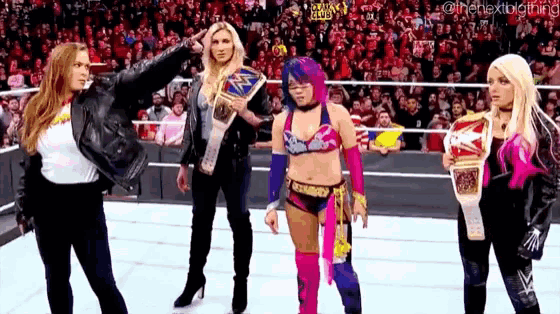 a group of female wrestlers are standing on a wrestling ring holding trophies .