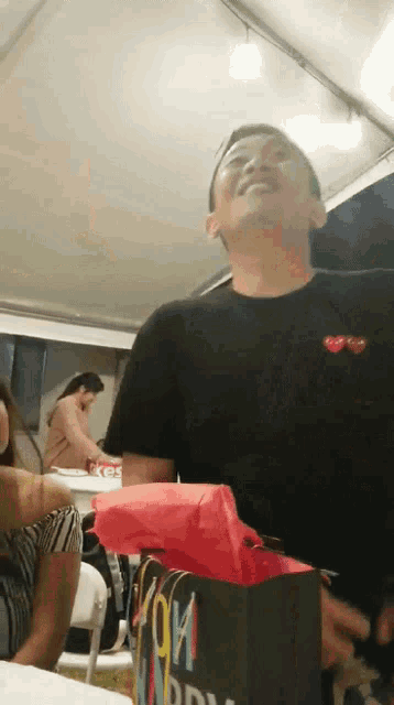 a man in a black shirt is holding a gift bag that says happy birthday on it