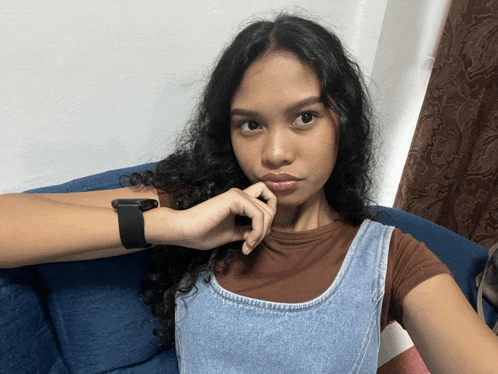 a woman wearing a watch takes a selfie on a blue couch