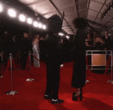 two people standing on a red carpet with one wearing a crown