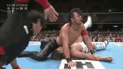 a wrestler is laying on the ground in a wrestling ring while another wrestler is standing behind him .
