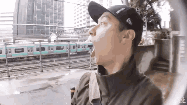 a man wearing a new era hat is standing in front of a train .