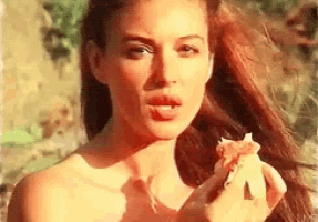 a naked woman is eating a piece of pizza outside .