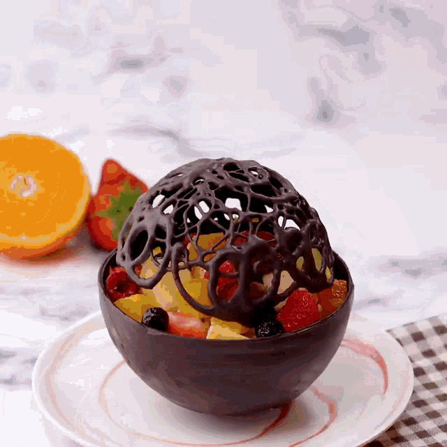 a chocolate bowl filled with fruit is on a white plate