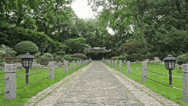 a stone walkway leading to a building in the middle of a lush green park