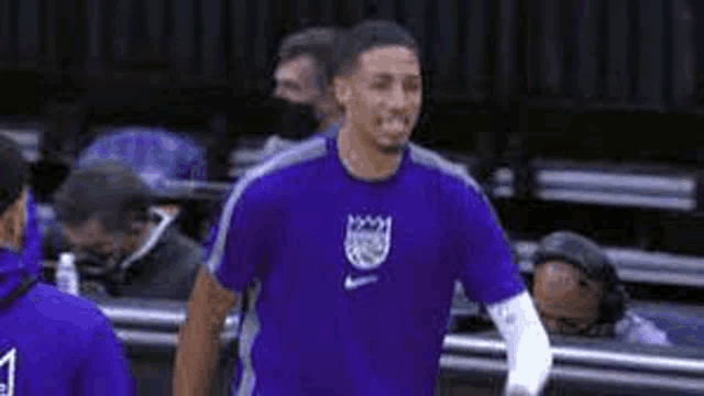 a basketball player is wearing a purple shirt and smiling while standing on a court .