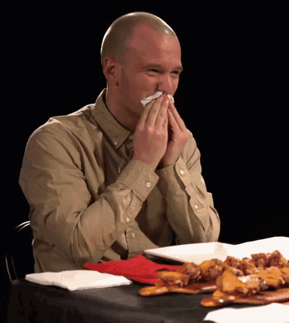a man wipes his nose with a napkin while sitting at a table with food
