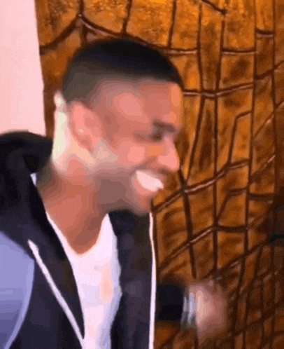 a man in a black jacket is smiling in front of a brown wall