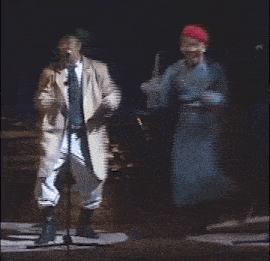 a man in a red hat stands next to a man in a blue robe