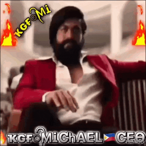 a man with a beard is sitting in a chair wearing a red jacket and a white shirt .