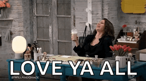 a woman is sitting at a desk holding a cup of coffee and saying love ya all .