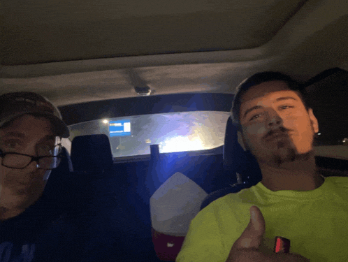 two men in a car with one wearing glasses and the other wearing a neon green shirt