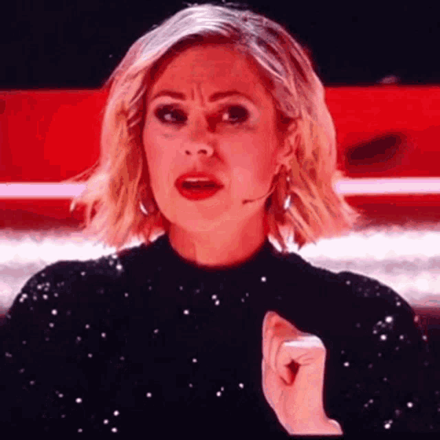 a woman in a black dress is making a funny face while holding her fist to her chest .