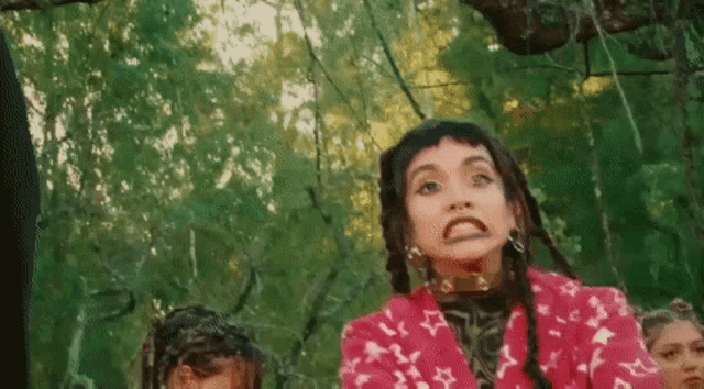 a woman in a pink jacket is making a funny face in front of a group of people in a forest .