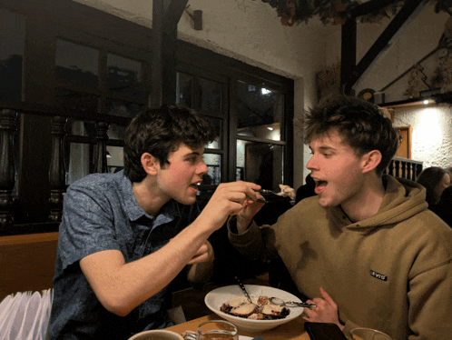 a man wearing a sweatshirt with the word life on it is feeding another man a bowl of food