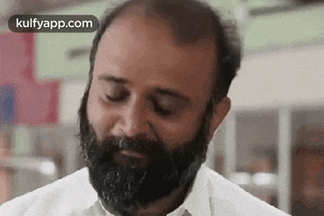 a bald man with a beard is wearing a white shirt and tie and making a funny face .