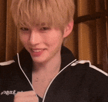 a young man with blonde hair is wearing a black jacket with white stripes .