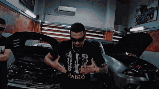 a man wearing a shirt that says pablo stands in front of a car