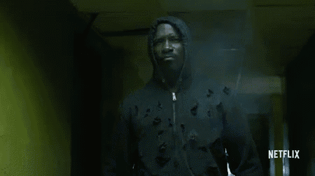 a man in a hoodie is walking through a hallway with bullet holes in the wall .